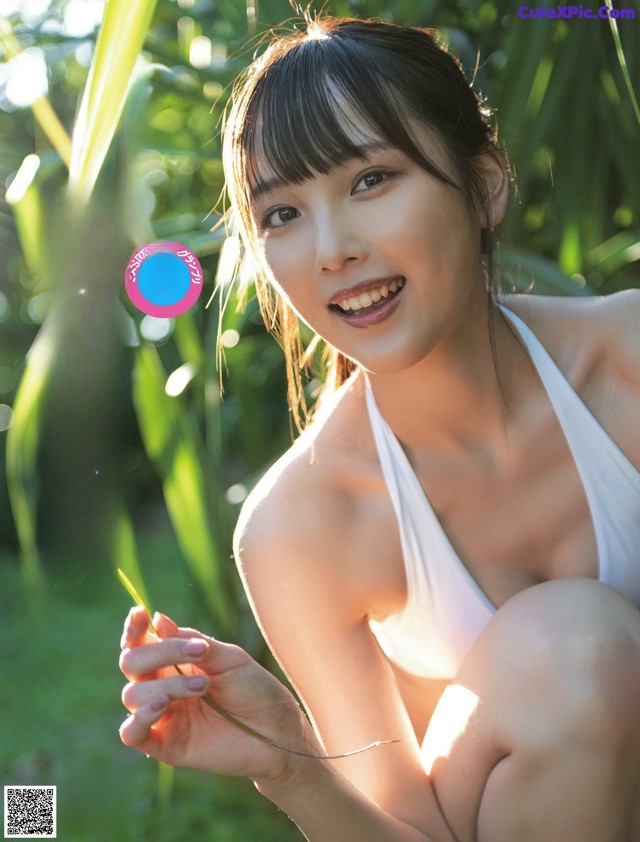 A woman in a white bikini sitting in the grass.