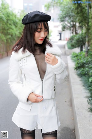 A woman in a white jacket and black stockings posing for a picture.