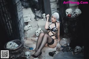 A woman in a black lingerie sitting on the ground next to skulls.