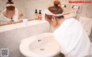 A woman in a white bathrobe brushing her teeth in a bathroom.