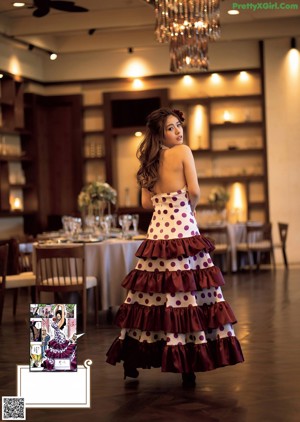 A woman in a blue top and pink skirt holding a book.