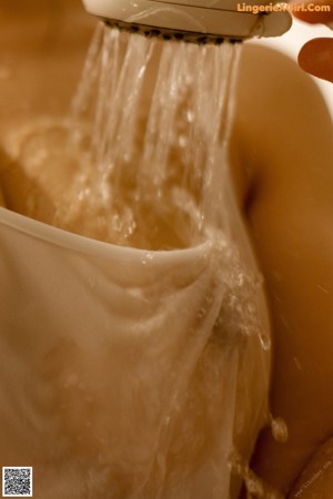 A naked woman sitting in a bathtub with water on her head.