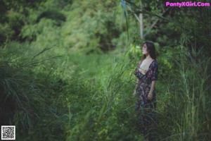 A naked woman standing next to a tree in the woods.