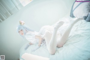 A woman with blue hair sitting on a bed.
