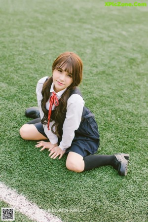 A young woman in a school uniform leaning against a window.