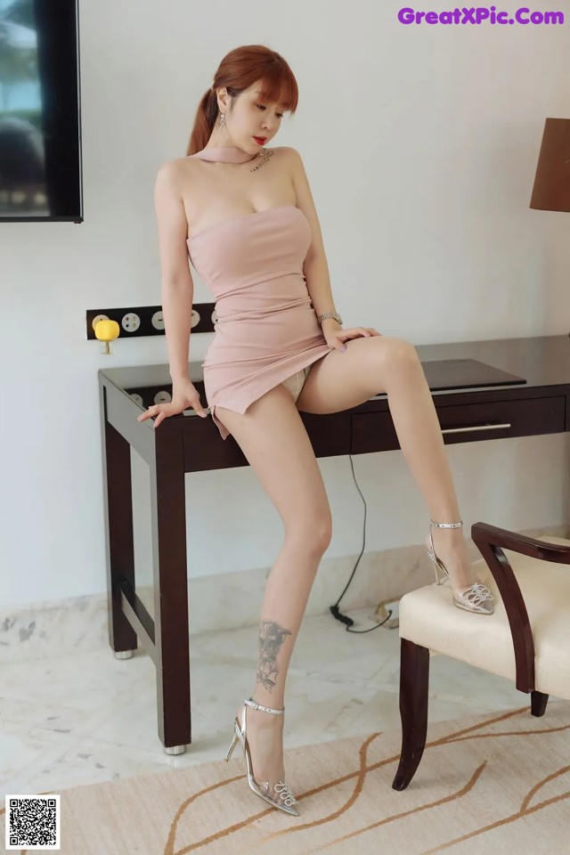 A woman in a pink dress sitting on a desk.