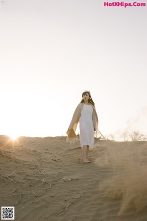 A woman in a white dress laying on a sand dune.