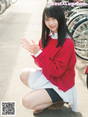 A woman in a red sweater and white skirt walking on a bridge.