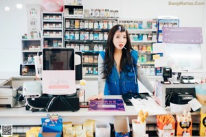 A woman crouching down in front of a refrigerator filled with snacks.