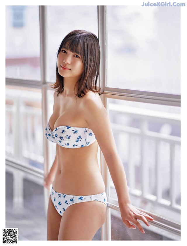 A woman in a white bikini standing by a window.