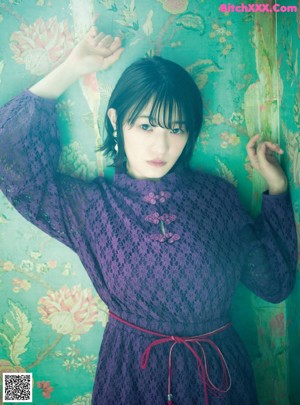 A woman in a kimono posing in front of a red wall.