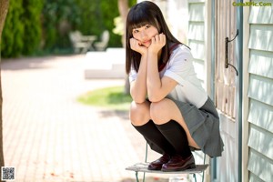A young woman leaning against a wall with a brown bag.