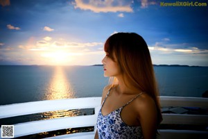 A naked asian woman posing on a balcony at sunset.