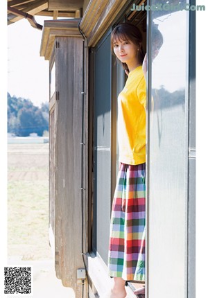 A woman in a red shirt and yellow plaid skirt holding a blue mop.