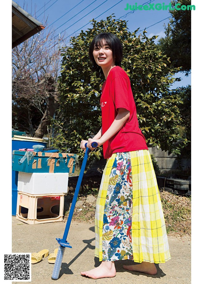 A woman in a red shirt and yellow plaid skirt holding a blue mop.