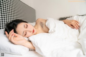 A woman in a white dress sitting on a bed.