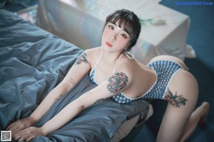 A woman in a blue and white polka dot bikini sitting on a bed.