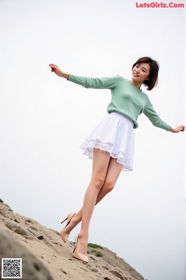A woman in a green sweater and white skirt standing on a rock.