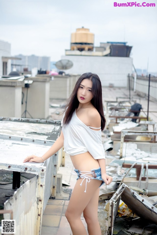 A woman in a white shirt and blue shorts posing on a roof.