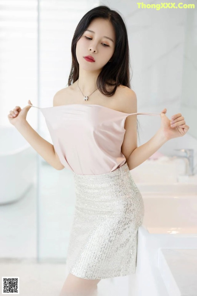 A woman in a pink top and silver skirt posing for a picture.