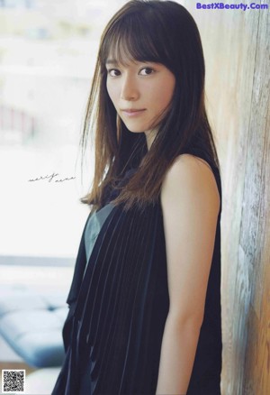 A woman with long brown hair and bangs leaning against a wall.