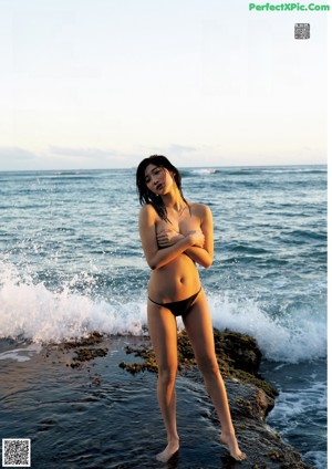 A woman in a black bikini sitting on the beach.